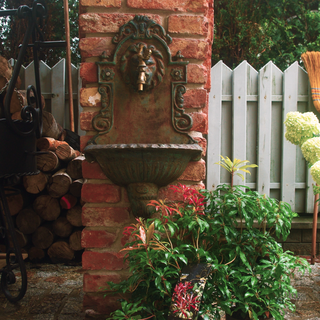 Ozdobny kran z lwem w ogrodzie, otoczony zielenią i stosami drewna, Apartamenty Agroturystyczne Papiernia, noclegi w górach