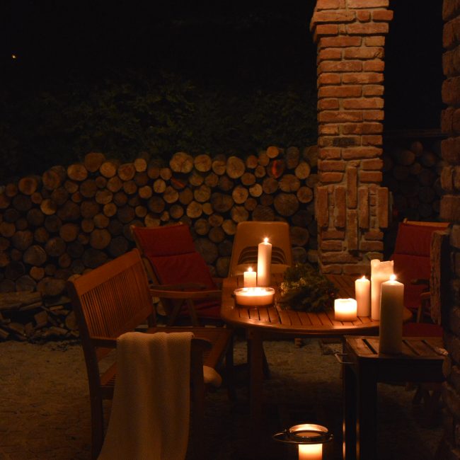 Tradycyjna biesiada góralska przy świecach w altanie, otoczony zielenią i stosami drewna, Apartamenty Agroturystyczne Papiernia, noclegi w górach. Romantyczny wypoczynek w górach