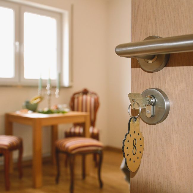 Wejście do apartamentu agroturystycznego z ręcznie malowaną grafiką wokół drzwi, widoczna stylowa jadalnia i klucz z góralskim brelokiem, klasyczny apartament, blisko Term Gorce